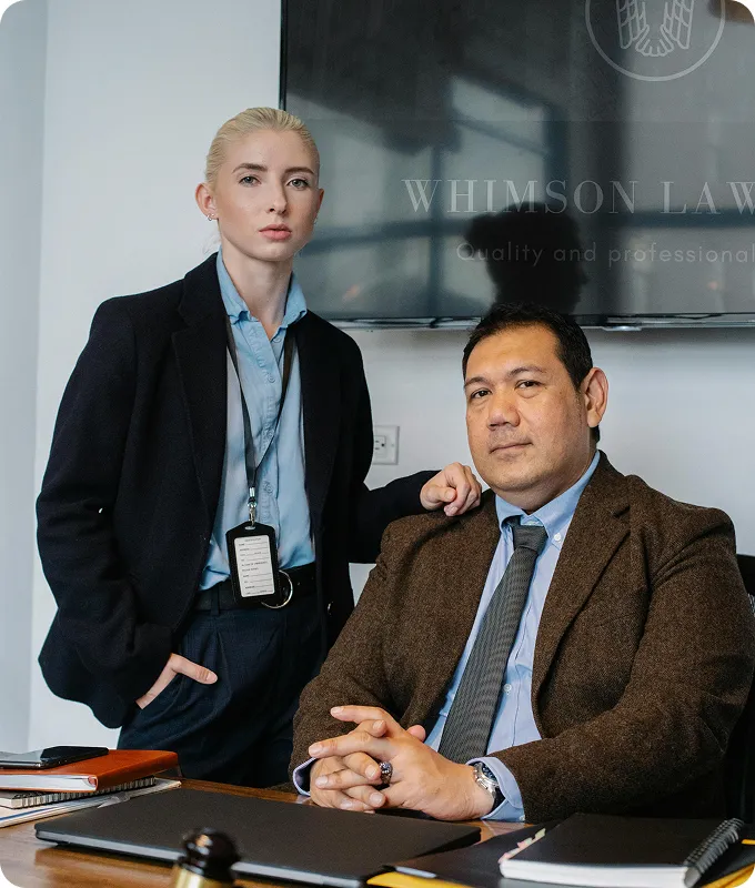 Two professional lawyers in business attire in an office with a Whimson Law sign in the background.